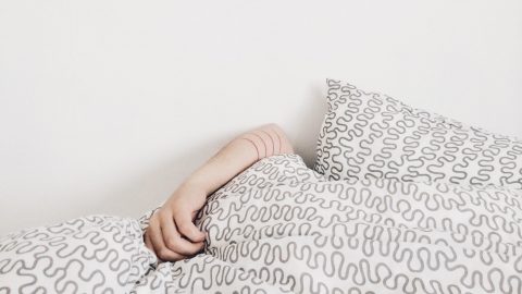 arm protrudes from stack of pillows and bedding