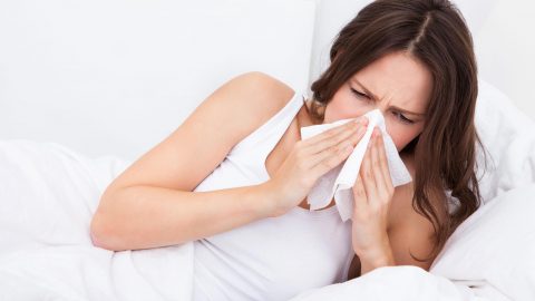 Woman is allergic to her pillow, blowing nose in Kleenex