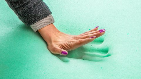 A woman's hand leaves an impression on a slab of memory foam