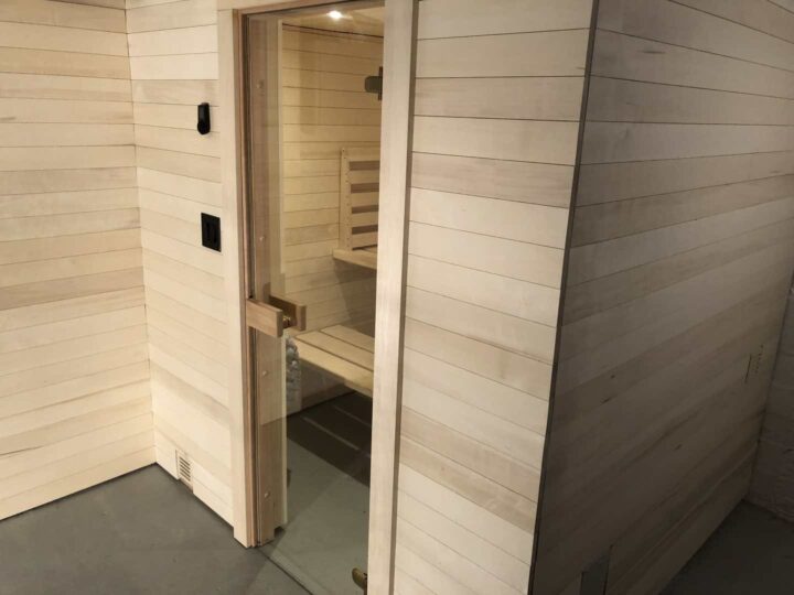 Exterior of a modern sauna with clear, blonde aspen paneling and glass door.